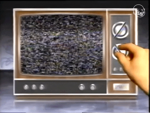 An old-school CRT TV with just static on the screen as a hand trys to tune to different stations